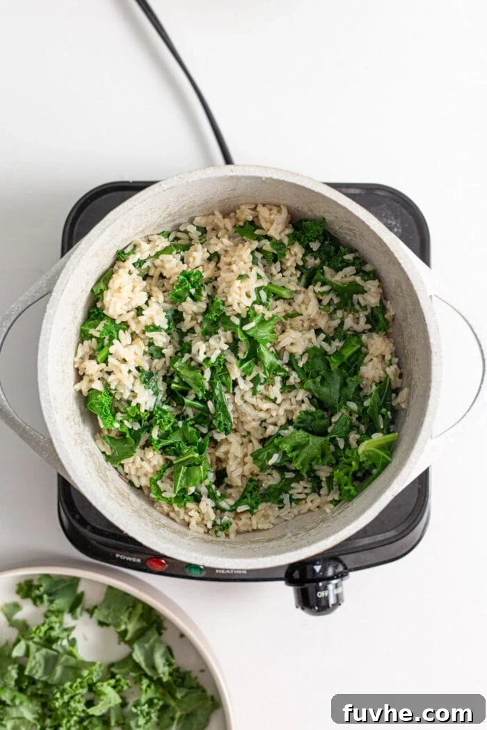 Pot of rice and kale being stirred together on a stovetop.