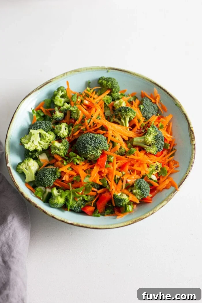 A colorful mix of chopped bell pepper, cucumber, carrot, broccoli, and fresh cilantro in a large bowl.
