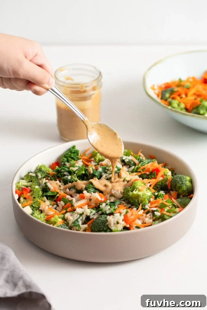A hand adding a spoonful of creamy peanut sauce to a vibrant kale and vegetable salad.