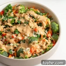 Bowl of kale broccoli brown rice salad topped with peanut sauce.