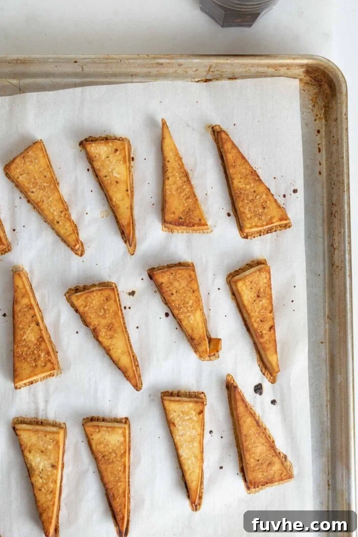 Golden-brown triangles of baked tofu arranged neatly on a parchment paper-lined baking tray, fresh from the oven and ready for the bowl.