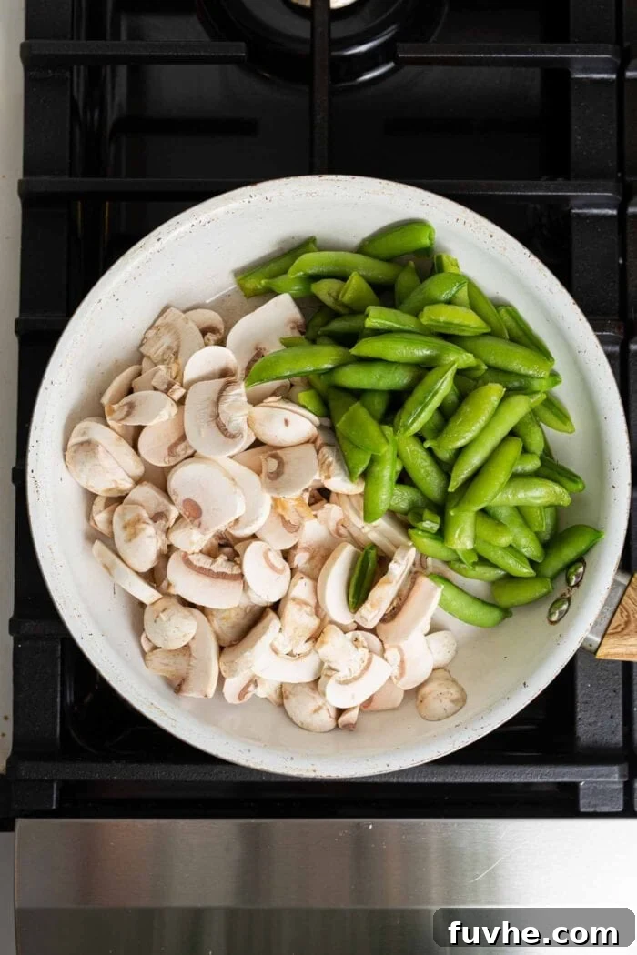 Freshly chopped mushrooms and bright green snap peas sizzling and cooking in a non-stick skillet on a gas stovetop, ready to be incorporated into the teriyaki quinoa bowl.
