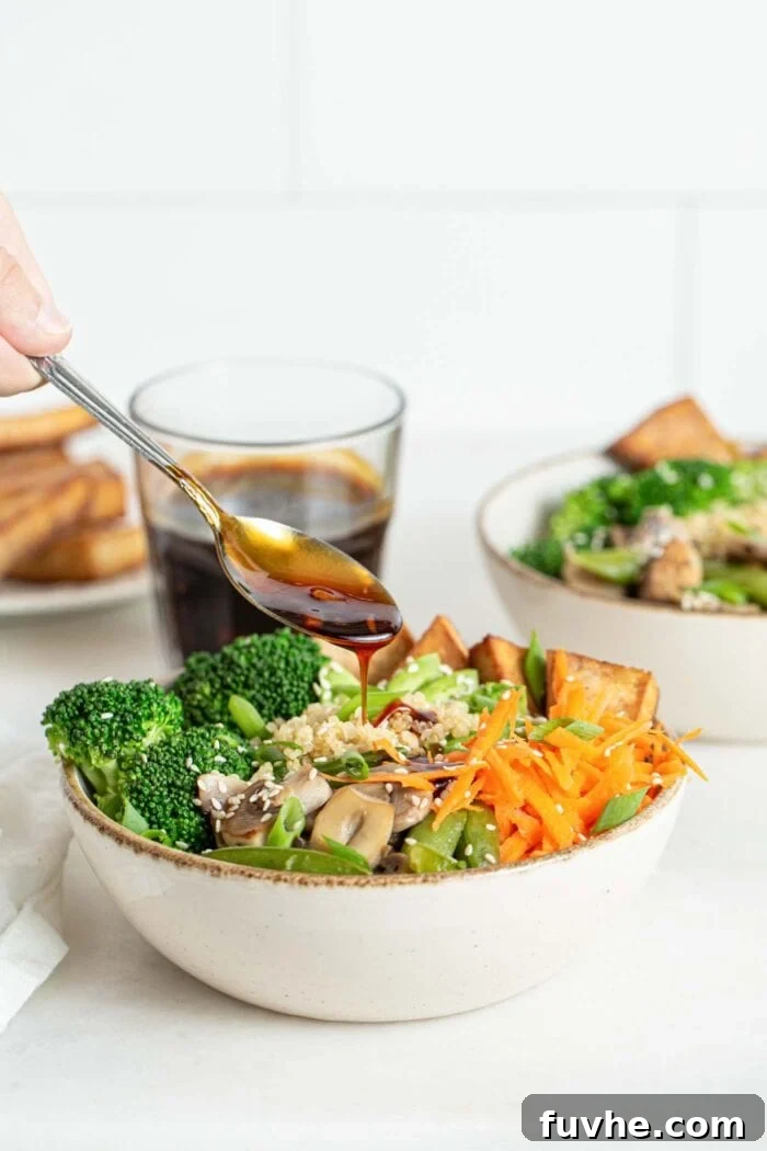 A spoonful of homemade teriyaki sauce gracefully falling onto a vibrant bowl filled with stir-fried vegetables and quinoa, adding the finishing touch to the meal.