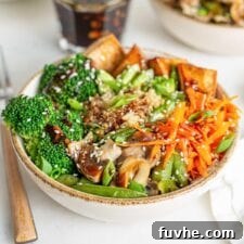 A vibrant, healthy vegan teriyaki quinoa and tofu bowl, beautifully garnished with fresh carrot, bright broccoli, and creamy avocado slices, highlighting a perfect meal prep option.