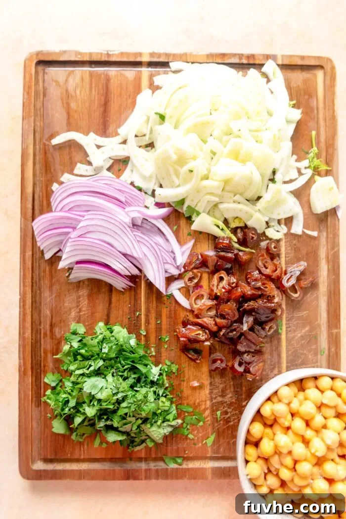 A cutting board with neatly chopped ingredients for freekeh salad: vibrant fennel, fresh mint and parsley, sweet dates, and thinly sliced red onion.