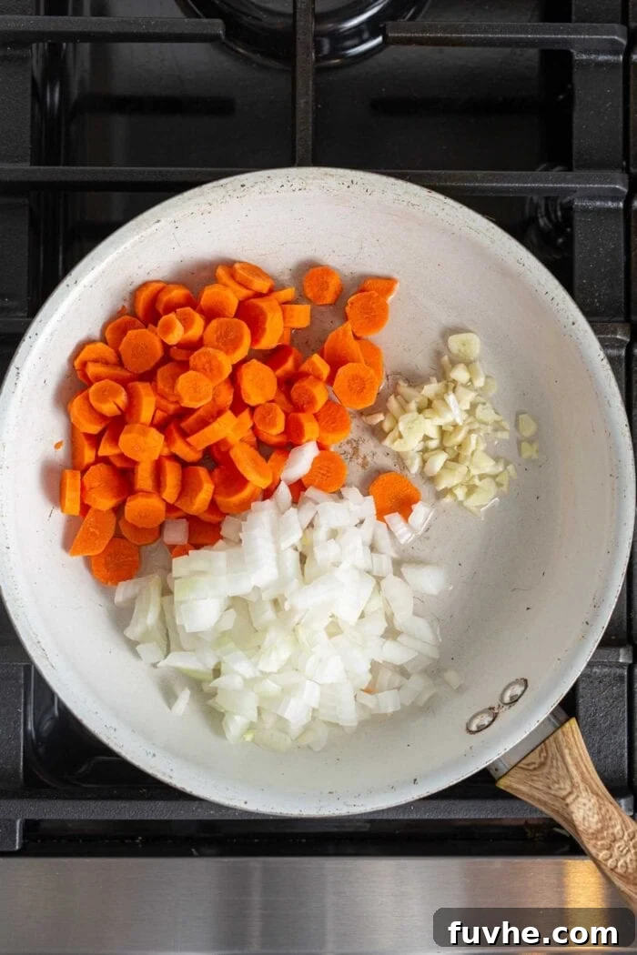 Creamy Vegan Panang Tofu Curry 4 Diced onions, garlic and carrot cooking in a skillet on a stovetop, starting to soften and become fragrant.