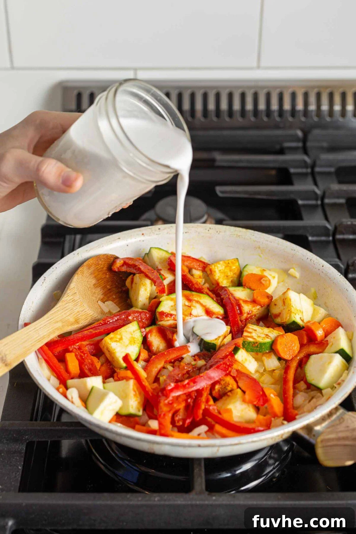 Creamy Vegan Panang Tofu Curry 6 Pouring coconut milk into a vegetable stir fry cooking on a stovetop, creating the creamy curry base.