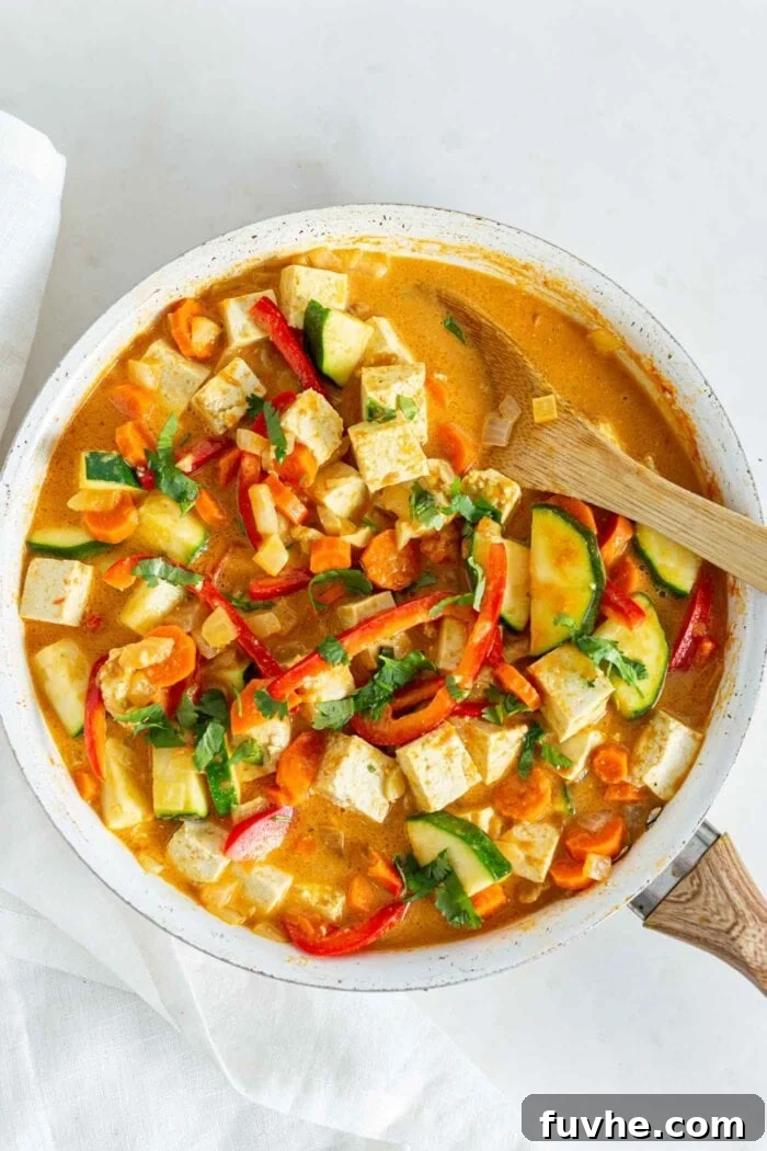 Creamy Vegan Panang Tofu Curry 7 Thick and creamy vegetable curry with tofu in a skillet with a wooden spoon, ready to be served.