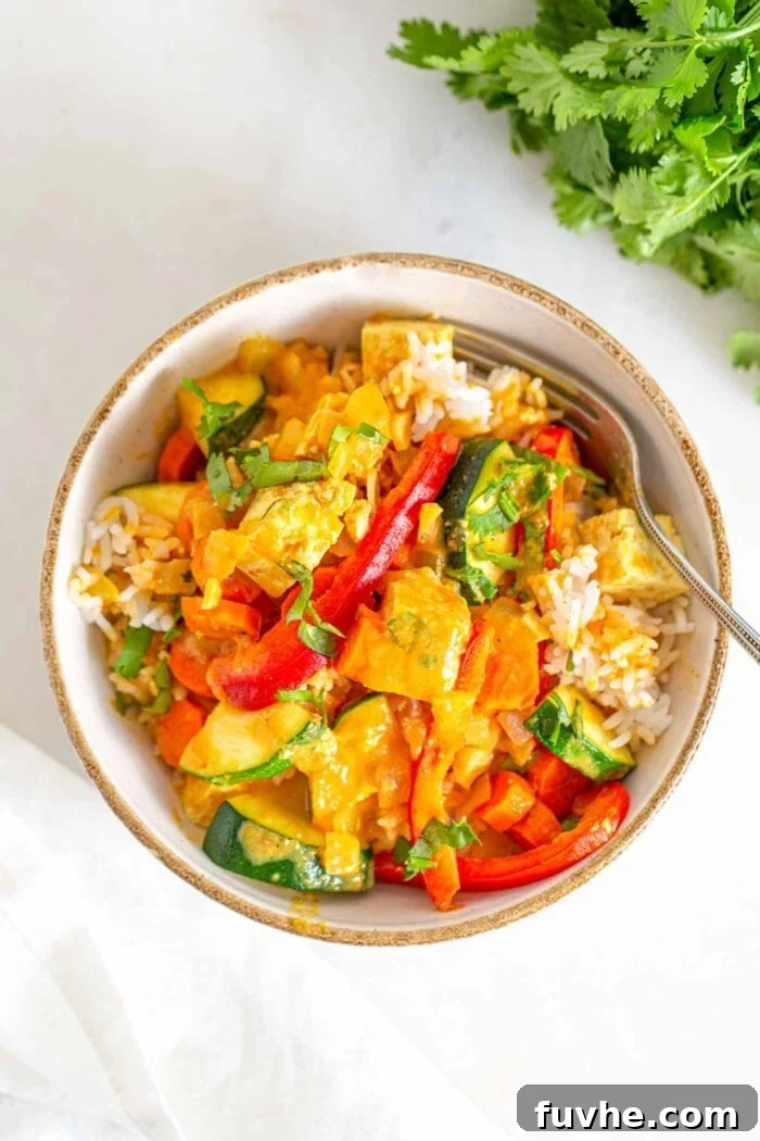 Creamy Vegan Panang Tofu Curry 8 A beautifully presented bowl of tofu vegetable curry over rice with fresh cilantro leaves beside it.