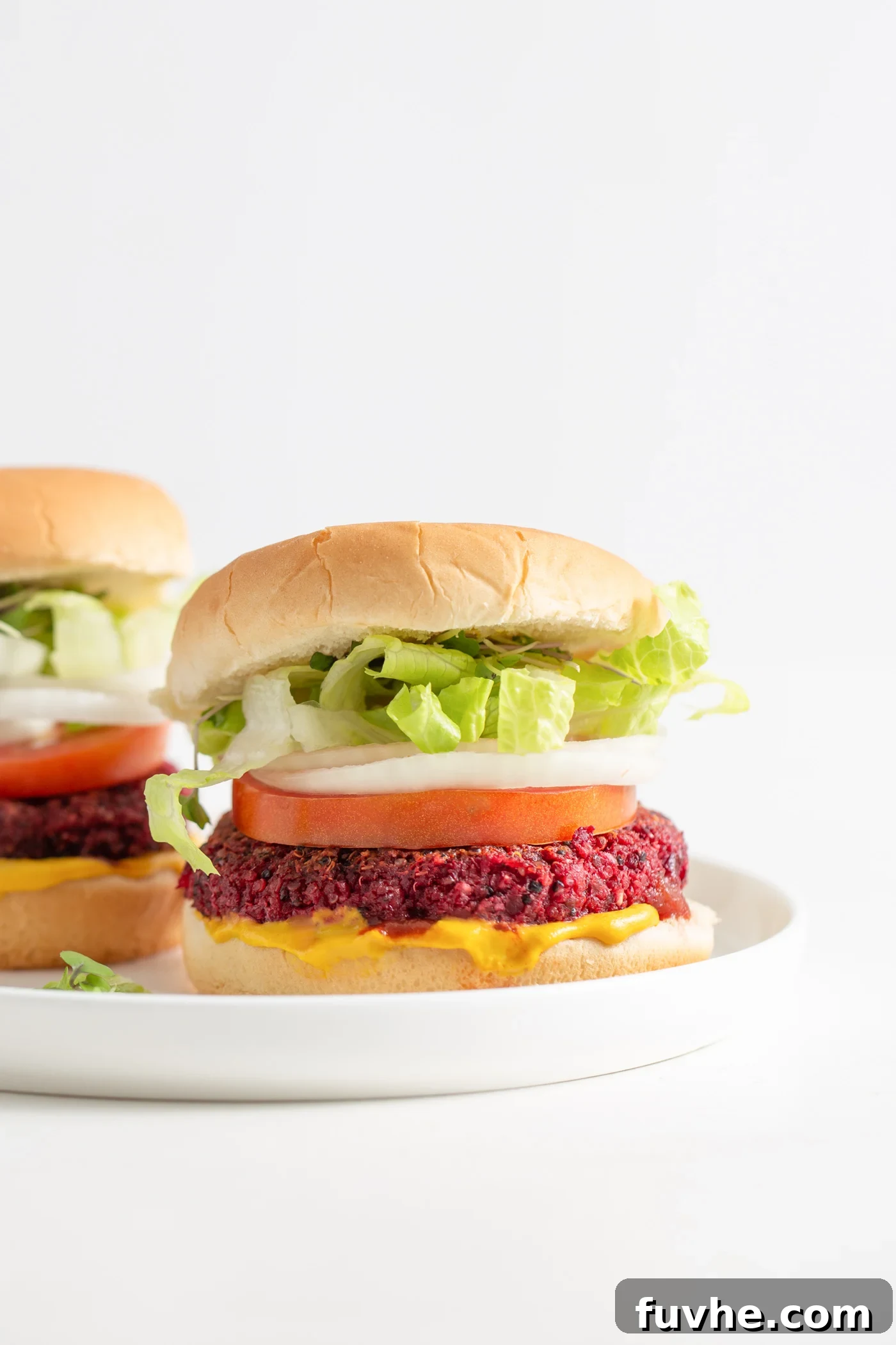 Two vibrant beet burgers served on toasted buns with crisp lettuce, fresh red onion, and ripe tomato slices, perfectly arranged and ready to be savored.