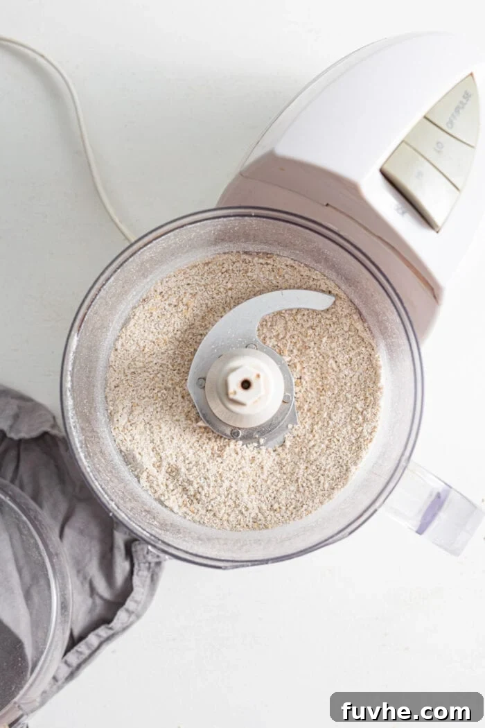 Rolled oats being efficiently processed into a coarse, grainy flour within a food processor, ready to be incorporated into the burger mixture.