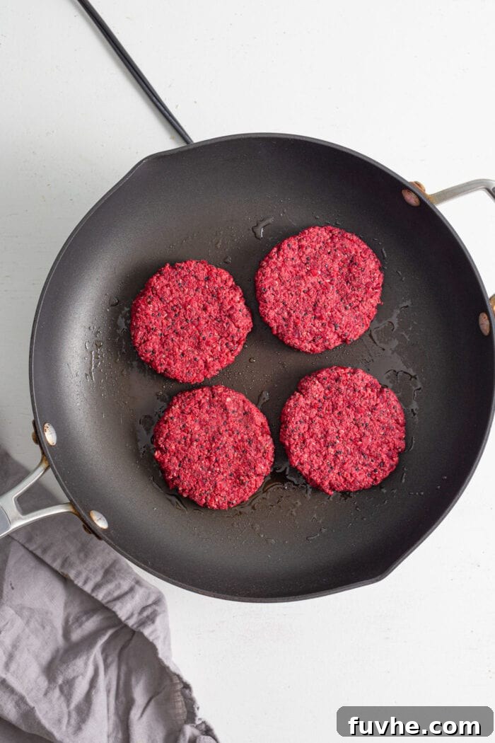 Four delicious vegan beet burgers sizzling and achieving a beautiful golden-brown crust in a hot non-stick skillet, ready to be flipped.