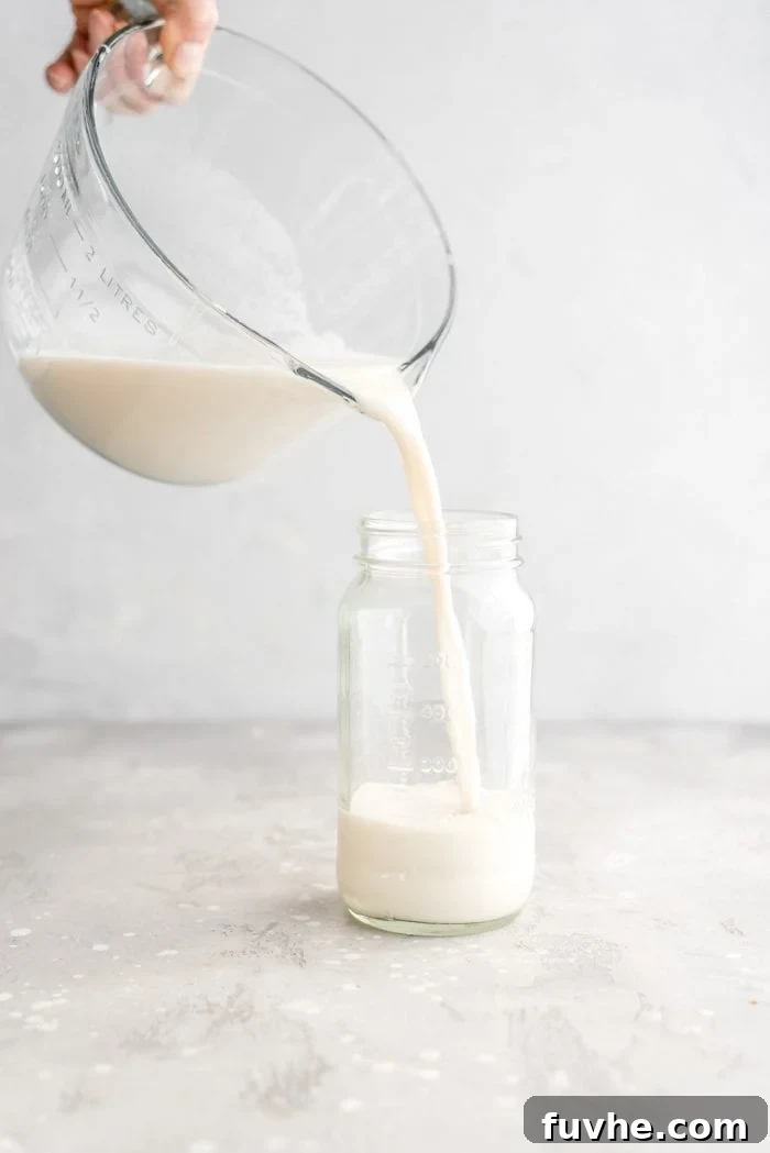 Pouring freshly made homemade oat milk into a glass storage container, highlighting its creamy texture.