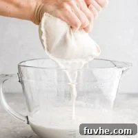 Straining the blended oat milk through a nut milk bag into a glass measuring cup.