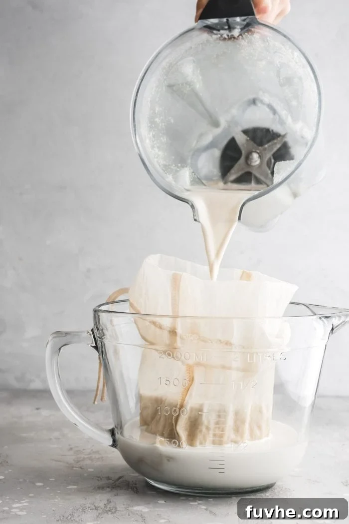 Pouring blended homemade oat milk into a nut milk bag set in a measuring cup, a crucial step for smooth milk.