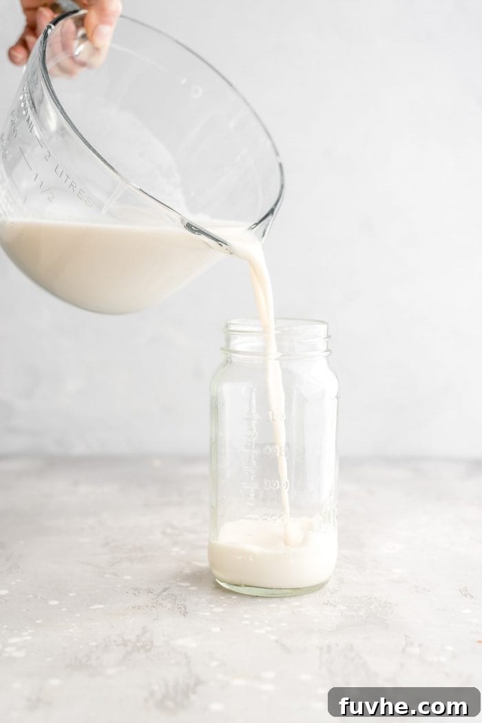 Pouring healthy, creamy homemade oat milk into a mason jar for convenient and airtight storage in the fridge.