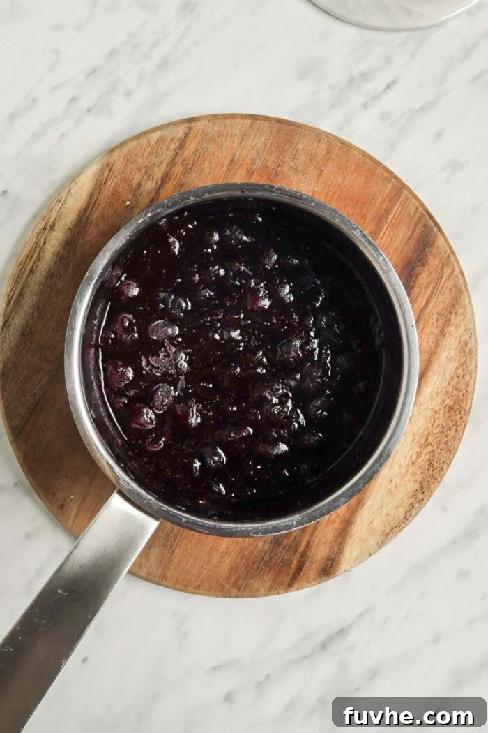 Whip Up Easy Berry Chia Seed Jam in Minutes 4 Mashed frozen blueberries in a small saucepan sitting on a cutting board, illustrating the first step.