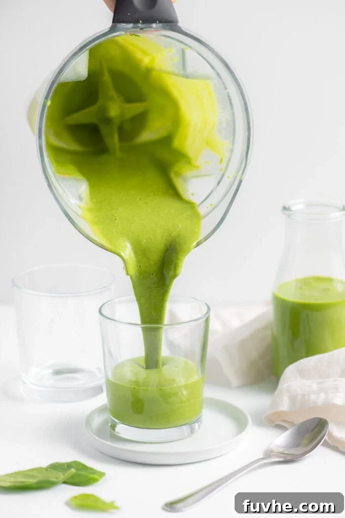 Kale and Apple Detox Smoothie 5 A stream of bright green kale spinach smoothie being poured from a blender into a clear glass, showing its smooth, rich consistency.