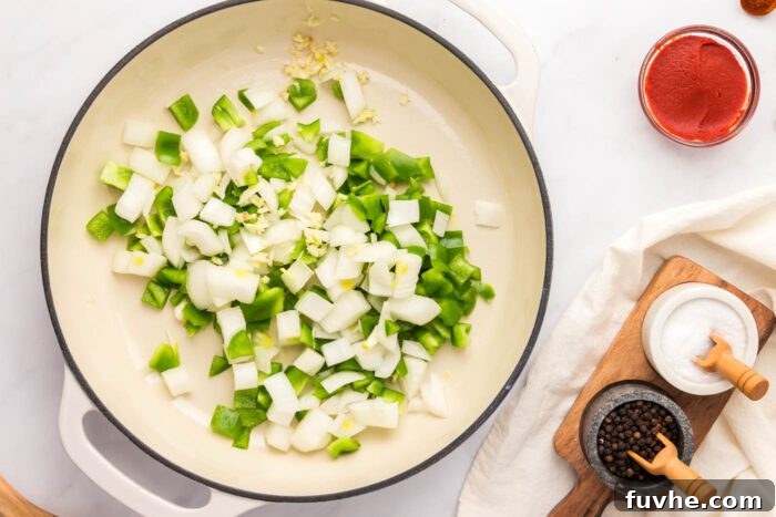 Diced onions, bell pepper, and minced garlic gently cooking in a saucepan, releasing their fragrant aromas.