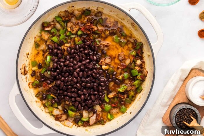 Black beans added to a saucepan containing the cooked bell pepper, onion, garlic, and fragrant spices, ready to simmer into a delicious BBQ mixture.