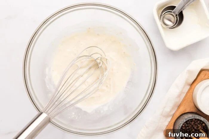 A smooth, creamy mayo-based dressing being whisked in a glass mixing bowl, ready for the vegetables.
