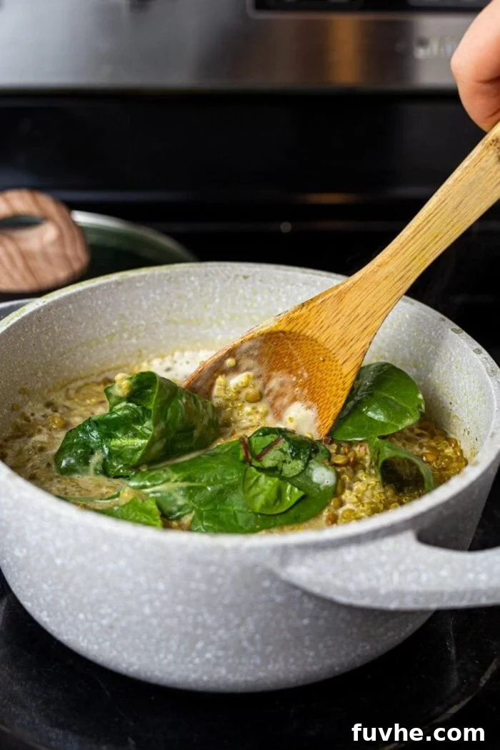Stirring spinach into a pot of cooked lentils and quinoa on the stovetop.