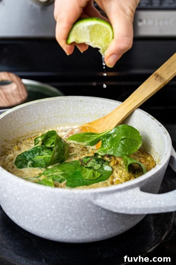 Squeezing lime juice into a pot of lentils, quinoa and spinach on the stovetop.