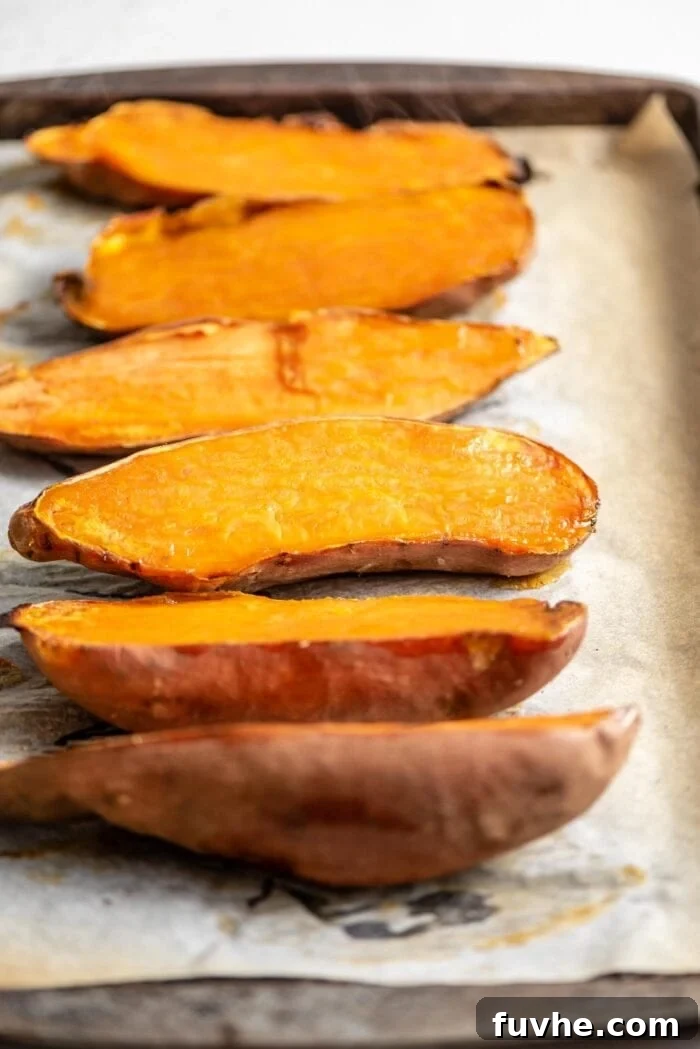 Six perfectly baked sweet potato halves, showcasing their caramelized edges, arranged neatly on a parchment-lined baking tray.