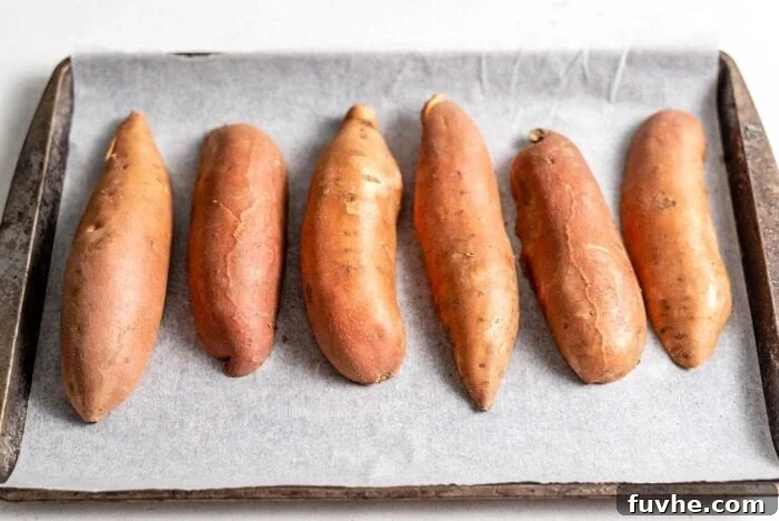 Six medium-sized sweet potato halves, with their cut sides facing down, arranged on a baking tray lined with parchment paper.