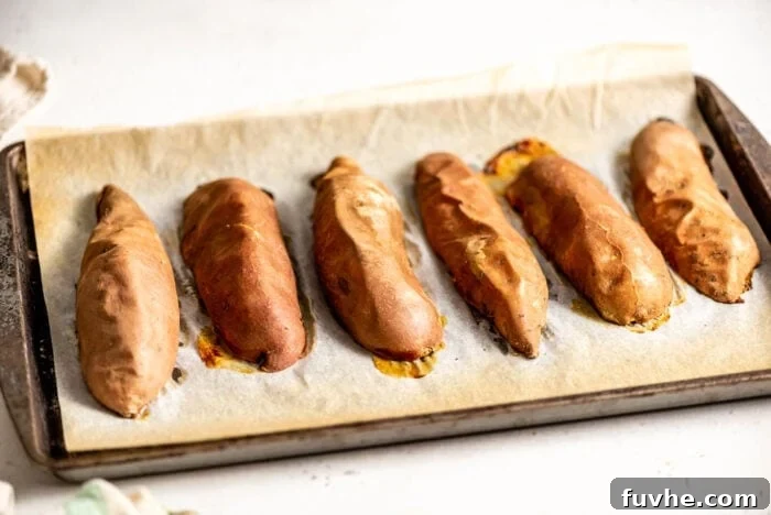Six golden-brown baked sweet potato halves on a baking tray, perfectly cooked and ready to be enjoyed, with their edges showing appealing caramelization.