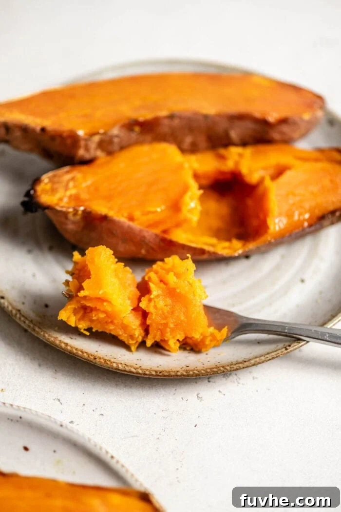 Two halves of a perfectly baked sweet potato on a plate, ready to be topped or enjoyed as is, with a fork beside it, highlighting its tender texture.