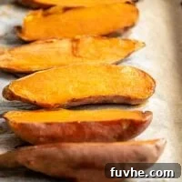 Six baked sweet potato halves, golden and caramelized, resting on a baking tray lined with parchment paper.