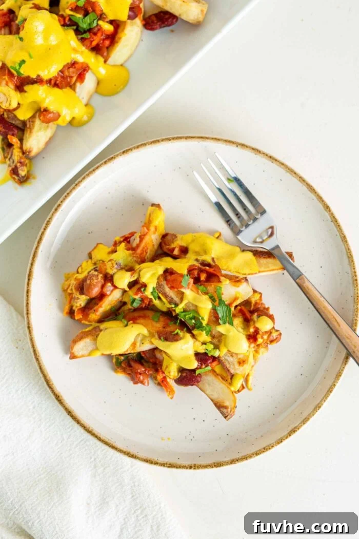 Ultimate Vegan Chili Cheese Fries 10 A small plate of baked fries topped with chili and cheese sauce, garnished for presentation.