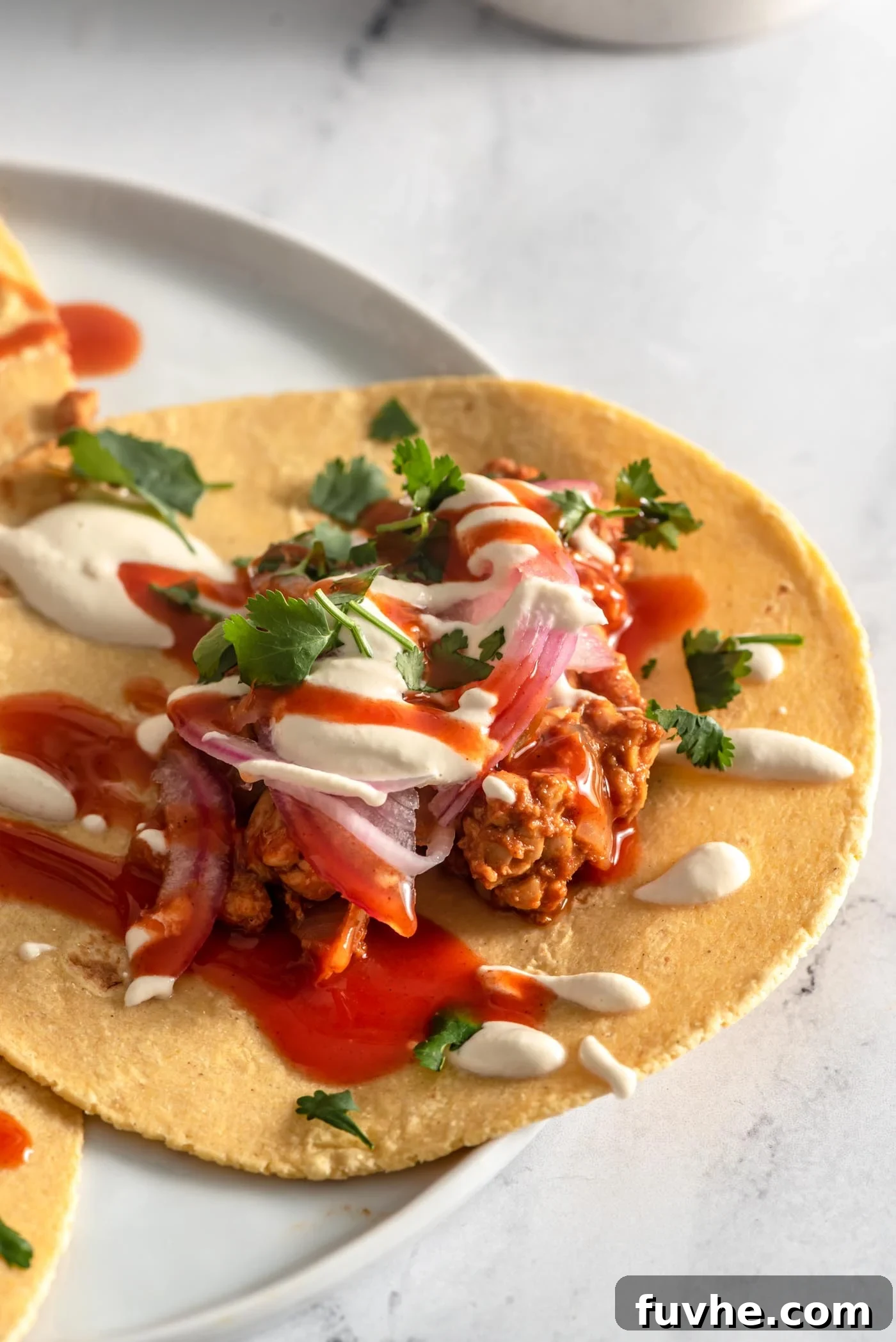 Savory Tempeh Tacos 2 Close up of a tempeh taco topped with vibrant pickled red onion, fresh cilantro, a drizzle of cashew cream sauce, and a touch of hot sauce.