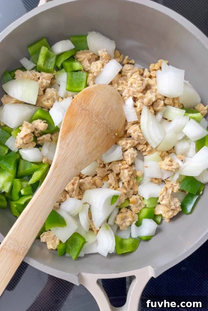 Savory Tempeh Tacos 5 Finely chopped onion, vibrant bell pepper, and crumbled tempeh sizzling and cooking in a pan.