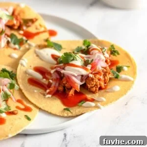 Three vegan tempeh tacos topped with pickled onion, cashew crema and hot sauce on a plate.