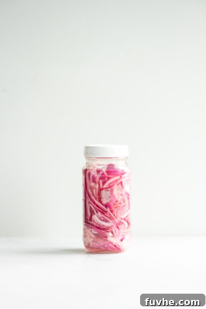 A sealed glass jar of bright pink quick pickled red onions, ready to be enjoyed.