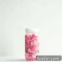 A sealed glass jar of quick pickled red onions against a white background.