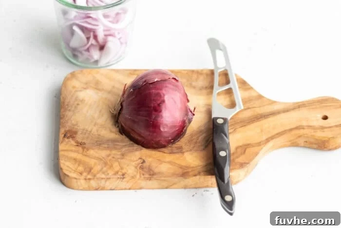 Half of a red onion on a cutting board with a knife, showing the first step of preparation.