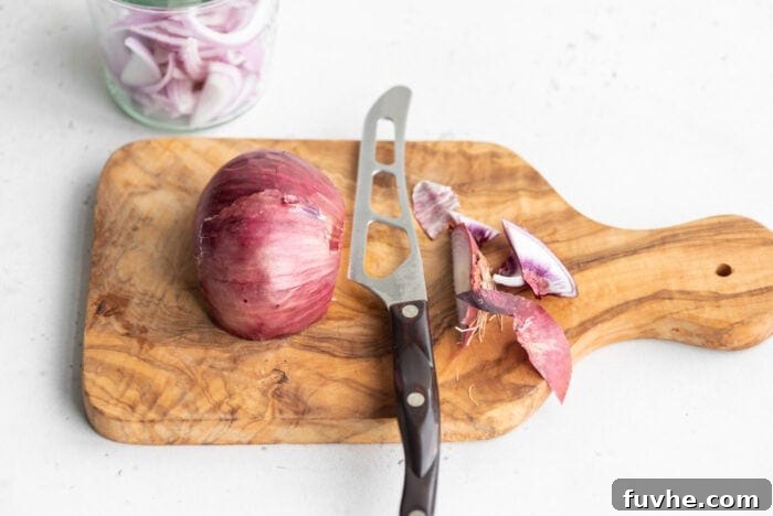 Half of a red onion with the ends neatly sliced off on a cutting board.