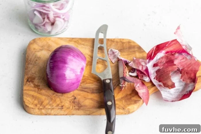 A peeled half of a red onion, clean and ready for slicing, on a cutting board.