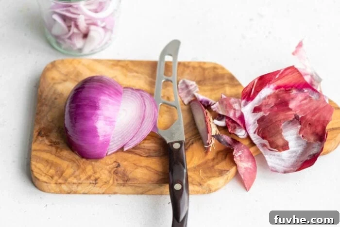A chef's knife thinly slicing a half of an onion on a cutting board.