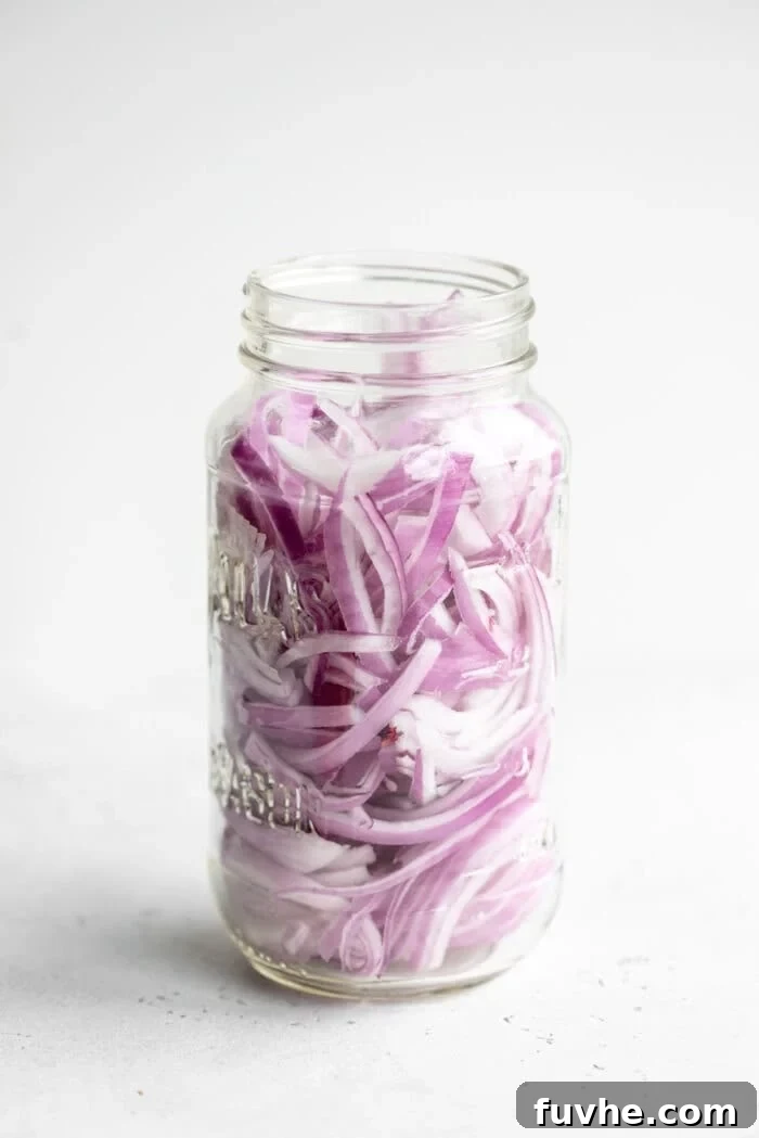 Raw red onion slices packed into a clear glass jar, awaiting the pickling liquid.