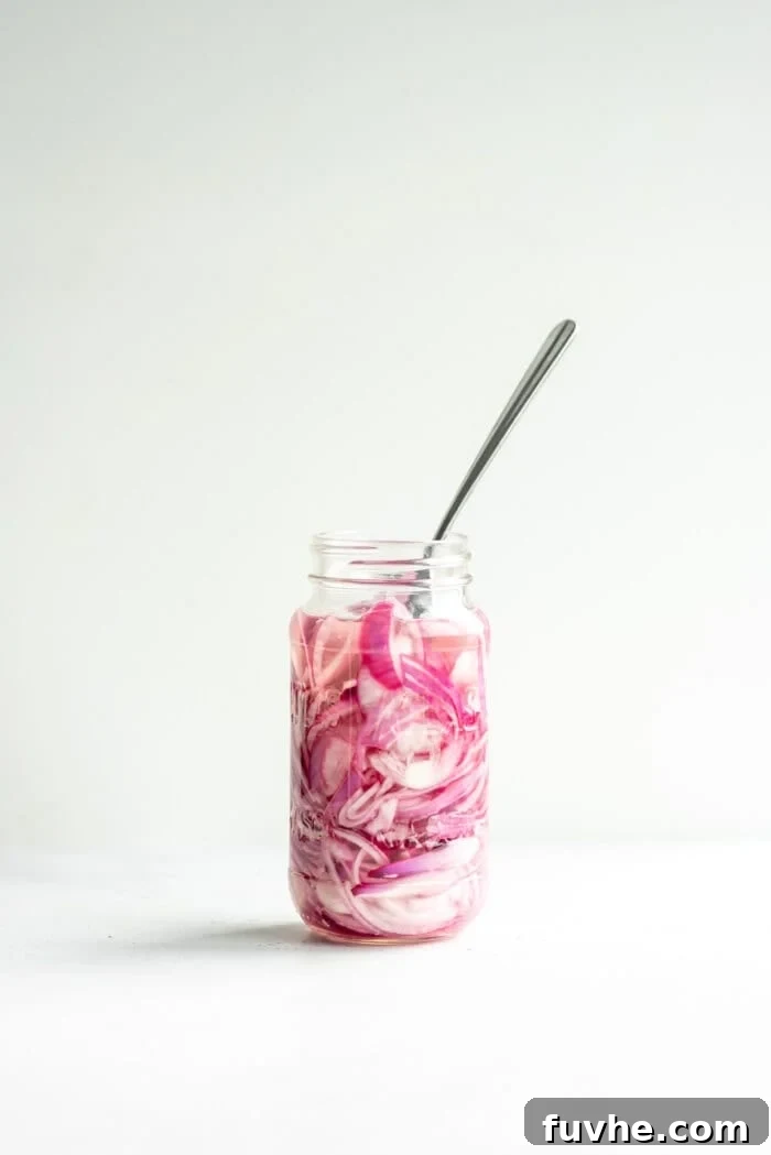A jar of sliced red onions with hot pickling liquid being poured over them.