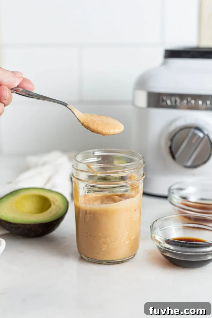 A spoon scooping a generous amount of homemade spicy cashew mayonnaise out of a small glass jar.