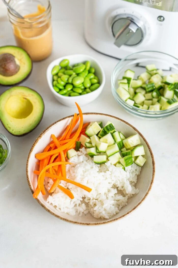 A bowl filled with cooked rice, alongside freshly prepared julienned carrots and diced cucumber, ready for assembly.
