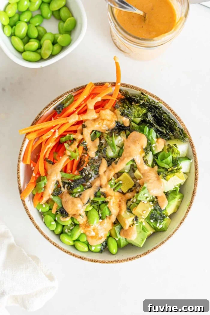 A finished vegan sushi bowl, artfully arranged with carrot, edamame, rice, cucumber, and nori, lavishly topped with spicy mayo and ready to eat.