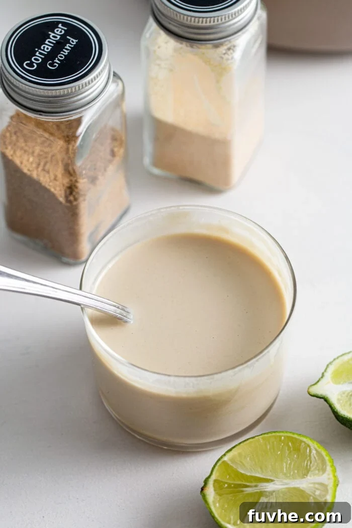 Creamy tahini dressing in a small glass with a spoon in it, ready to be drizzled over a salad.