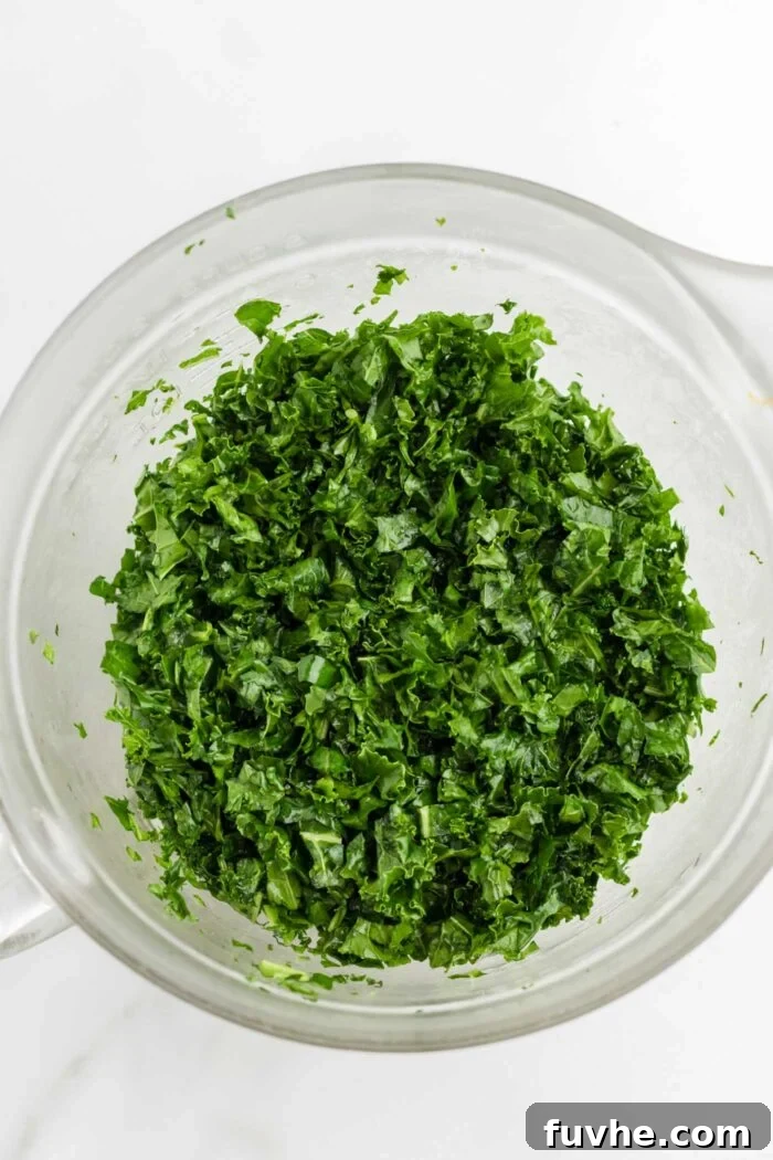 Chopped kale that's been massaged in oil, in a large glass mixing bowl, looking softened and dark green.