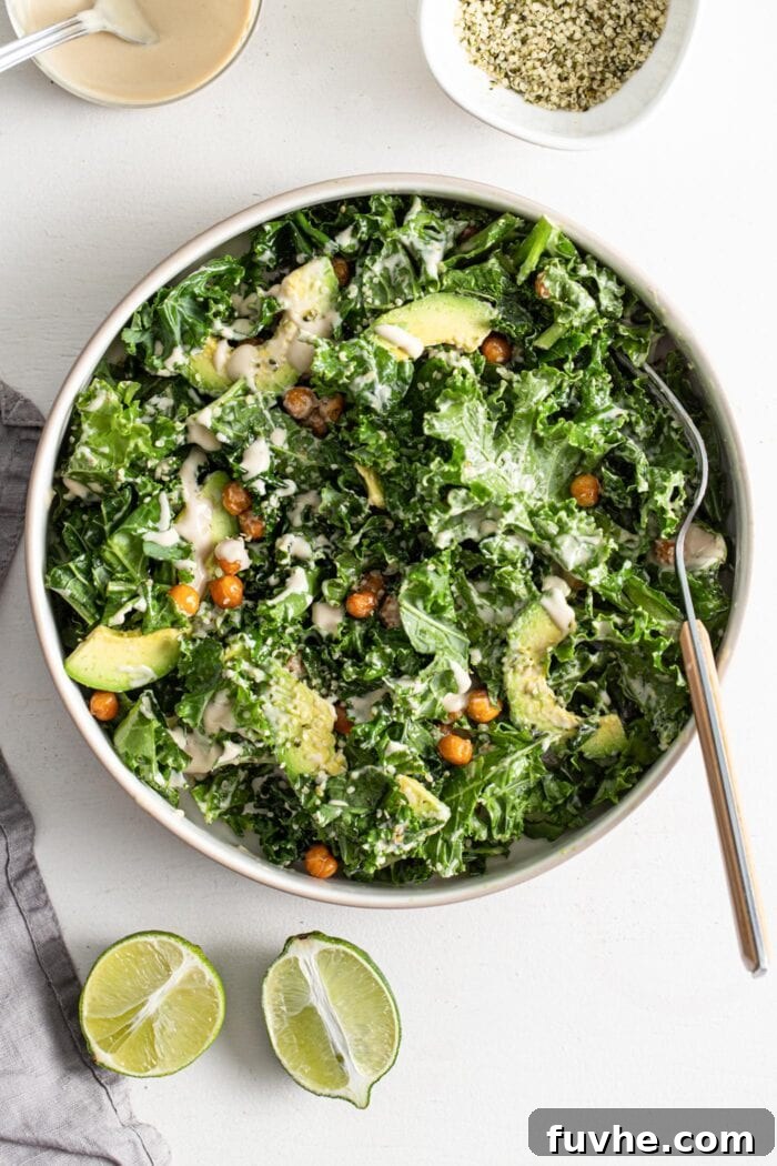 A vibrant bowl of kale salad with chickpeas, creamy avocado, and hemp seeds, generously coated in a tahini dressing.